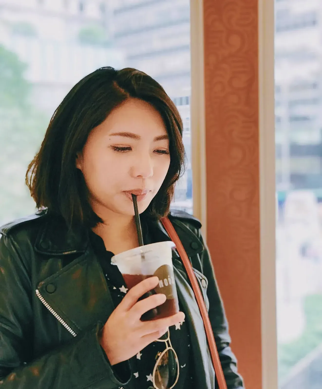 Woman in casual setting drinking coffee and taking a selfie with her cellphone.