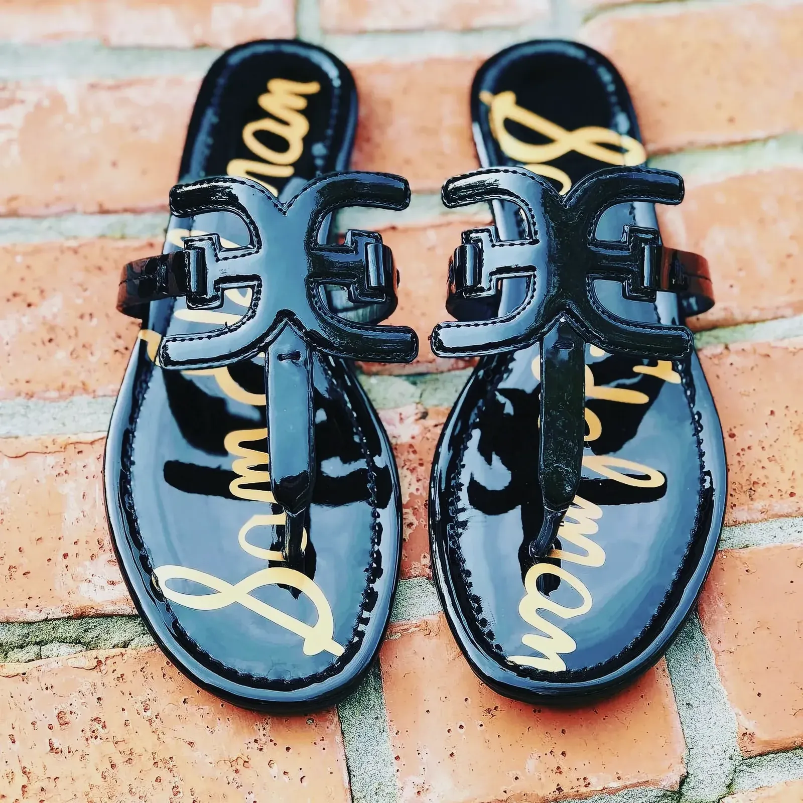 Stylish Sam Edelman black sandals with gold logo on a brick surface