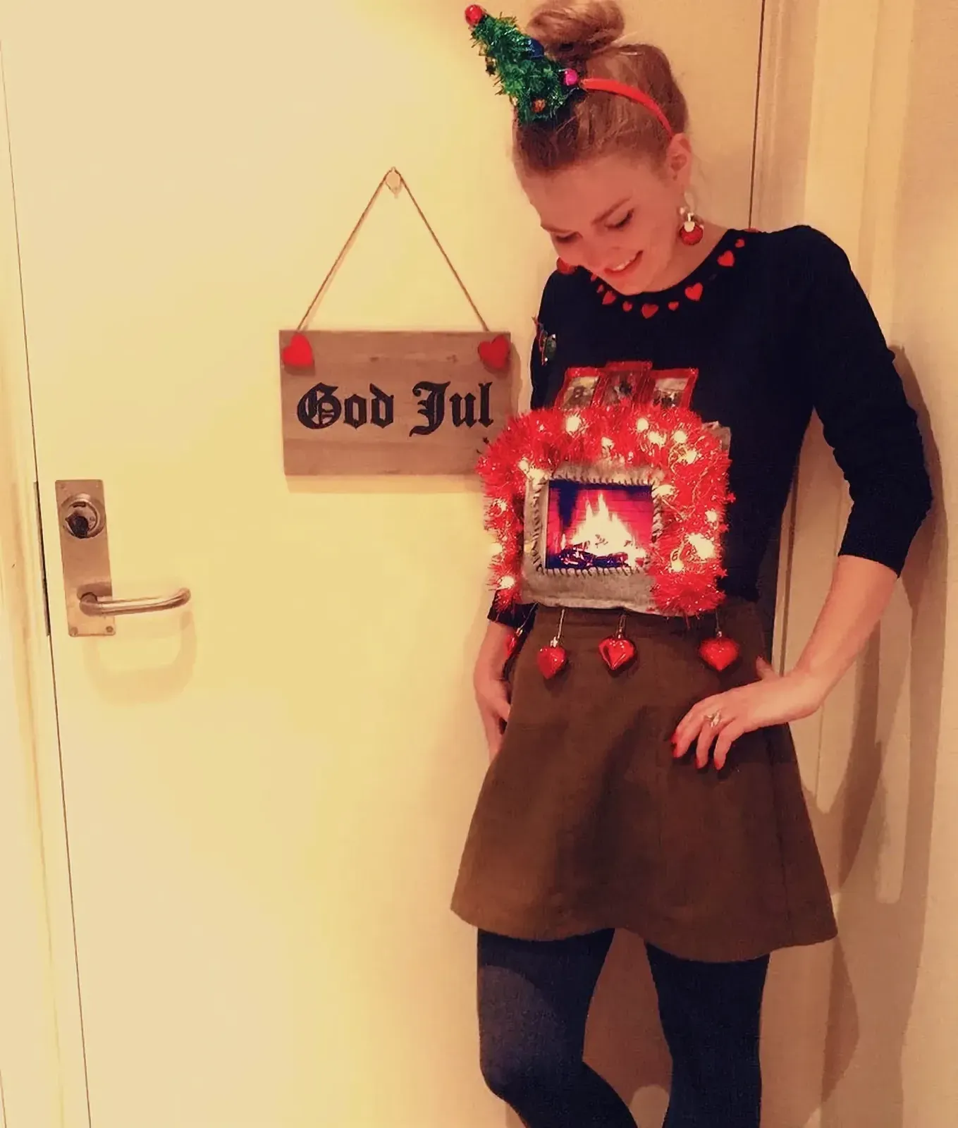 Woman wearing a distinctive Christmas sweater with a fireplace design and a Christmas tree headband