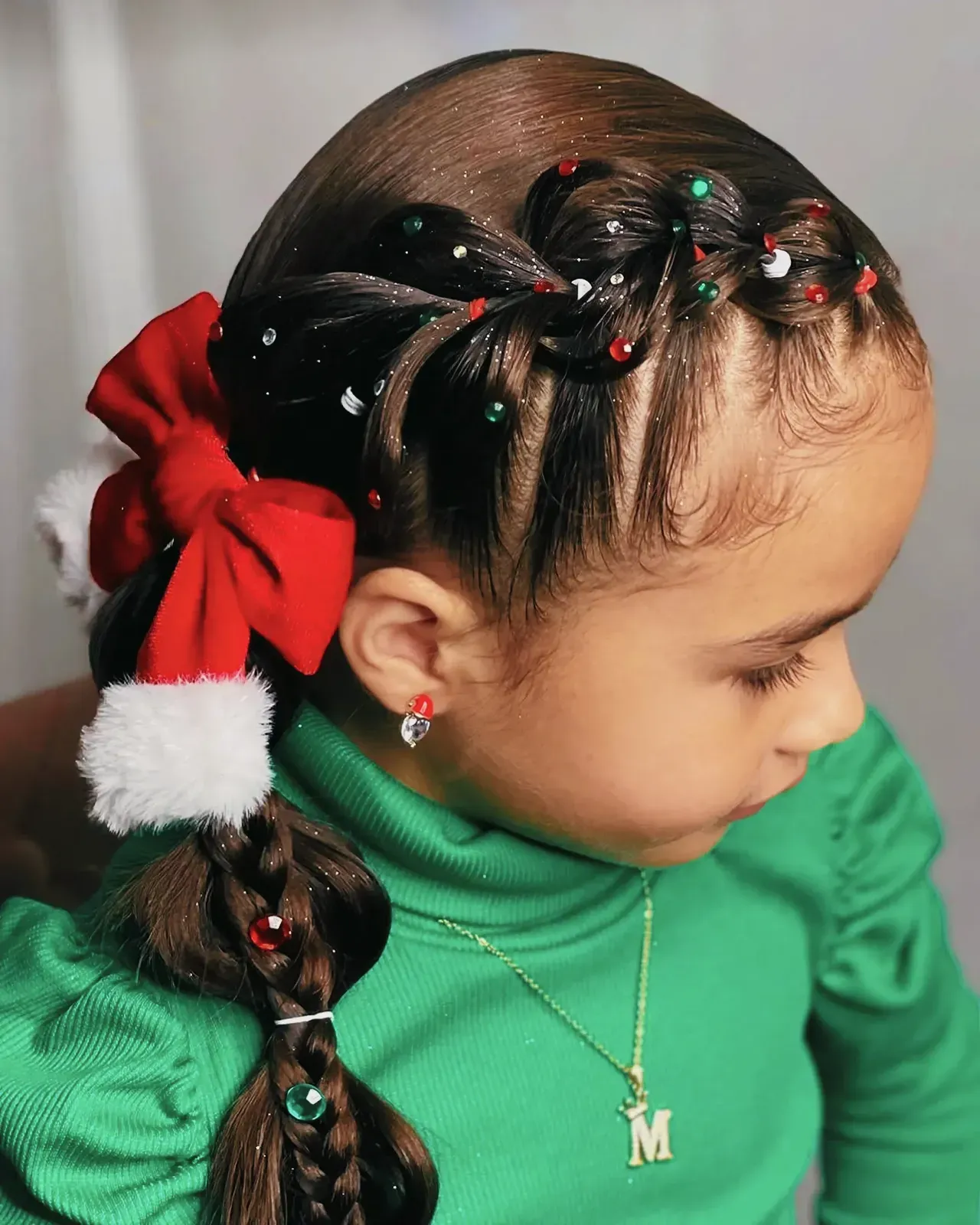 Young girl with beautiful Christmas hairstyle adorned with a red bow and colorful beads.