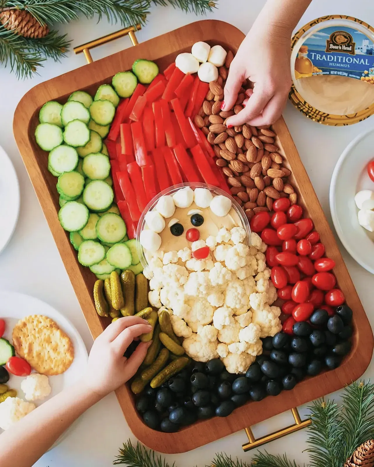 Santa-themed charcuterie board with fresh vegetables, fruits, hummus, and more.