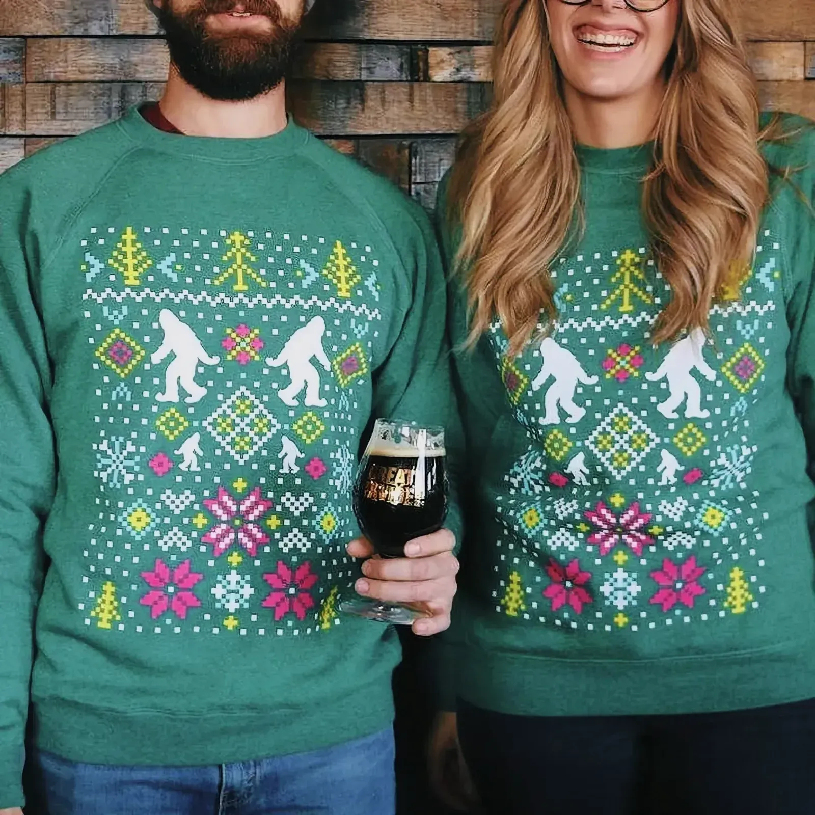 A couple wearing green sweaters smiling and holding glasses of beer.