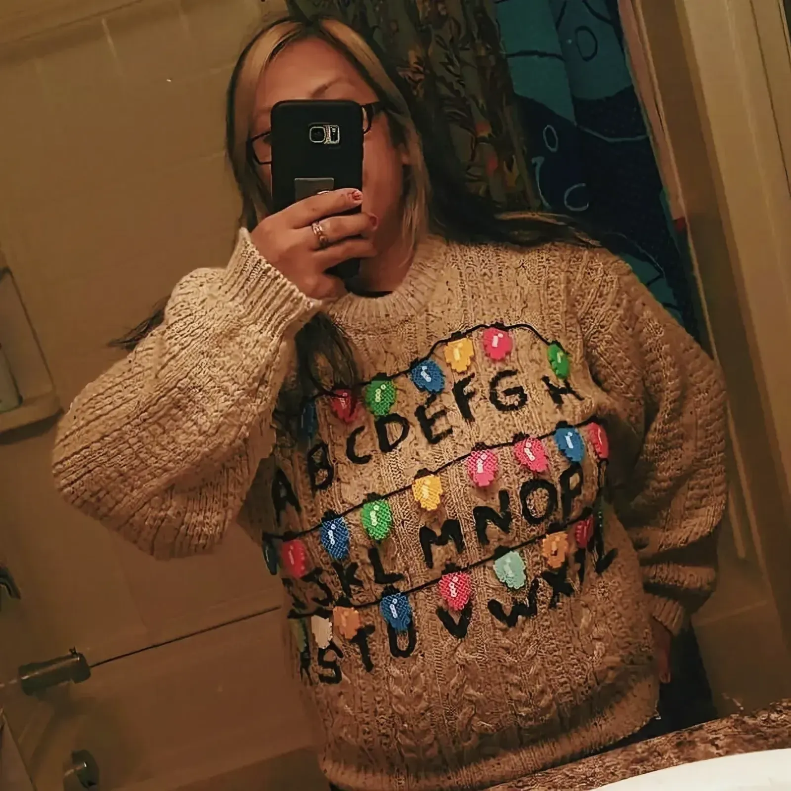 Fashionable woman taking a selfie in a mirror with a handmade ugly Christmas sweater