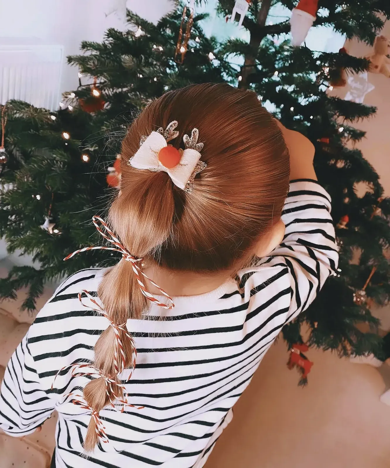 Young girl with festive Christmas hairstyle near a decorated Christmas tree