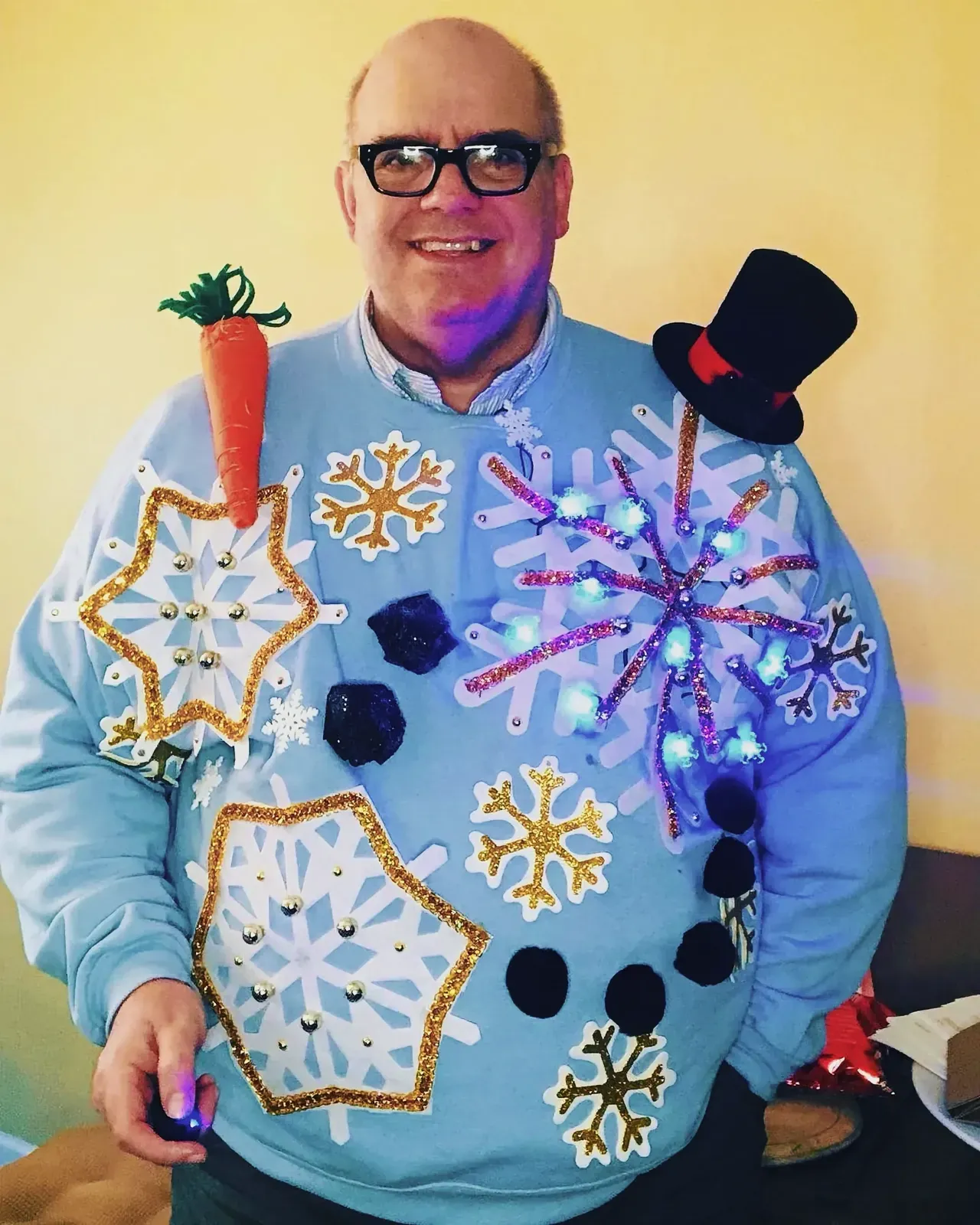 Cheerful man wearing a unique sweater adorned with snowflakes and carrots.