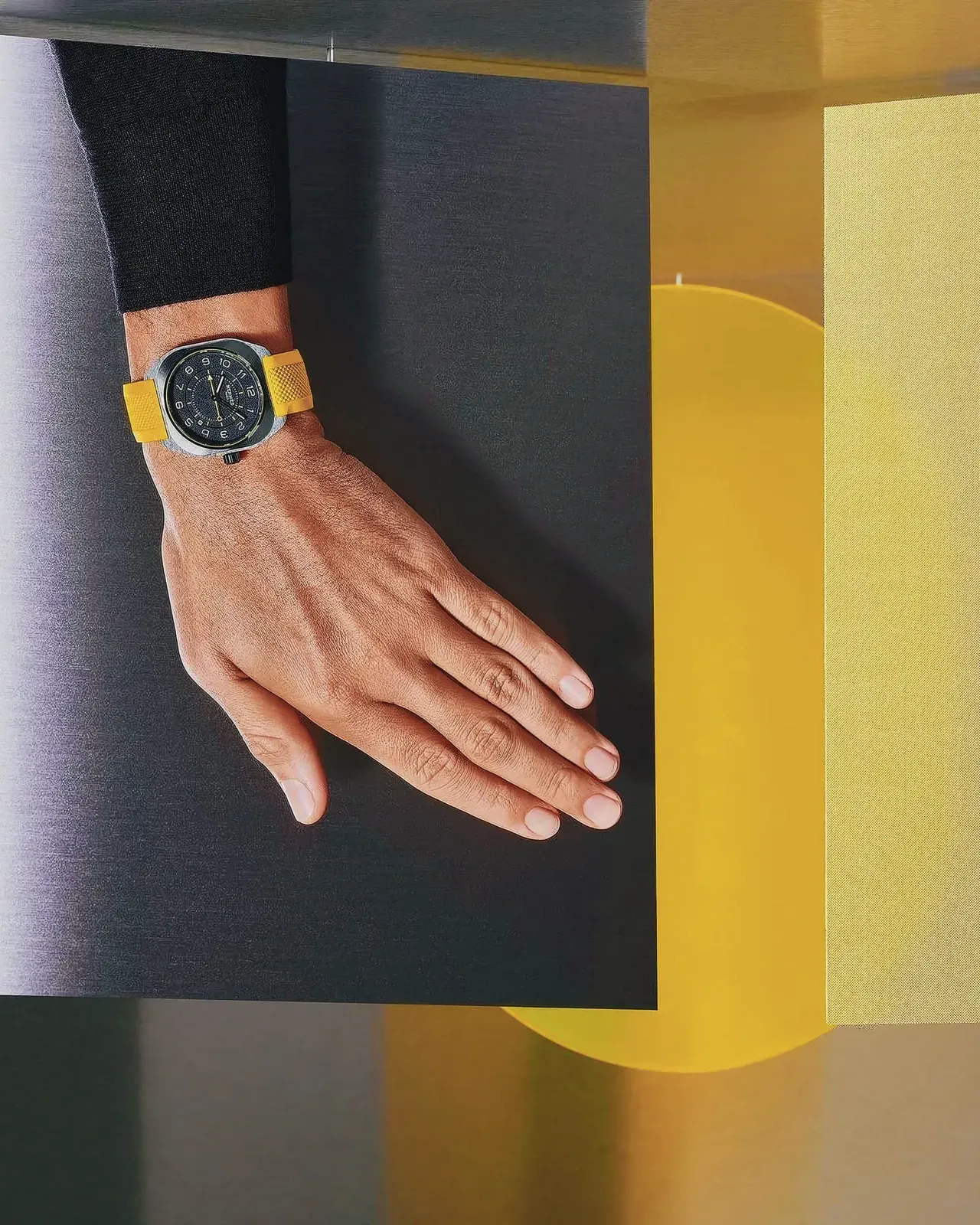 Close-up view of a human hand with a yellow watch on a black surface