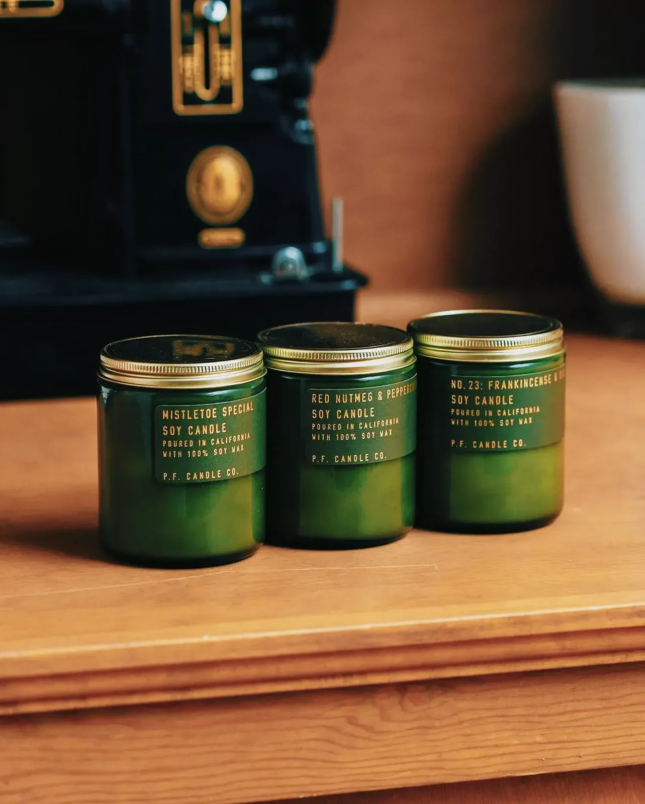Green glass vessels with gold lids and kraft labels housing winter scented candles