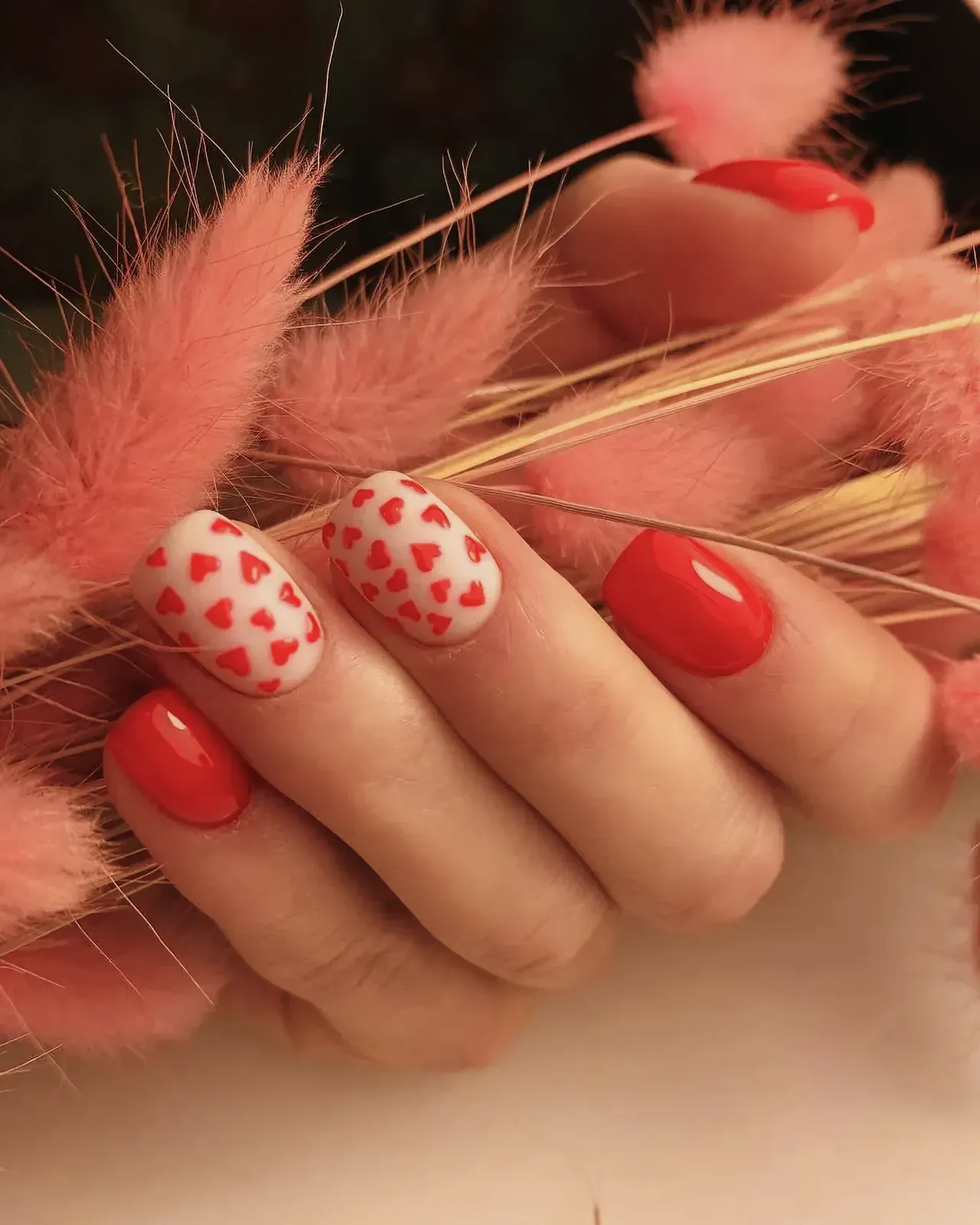 Close-up of Valentine's Day manicure with pink nail polish and red hearts