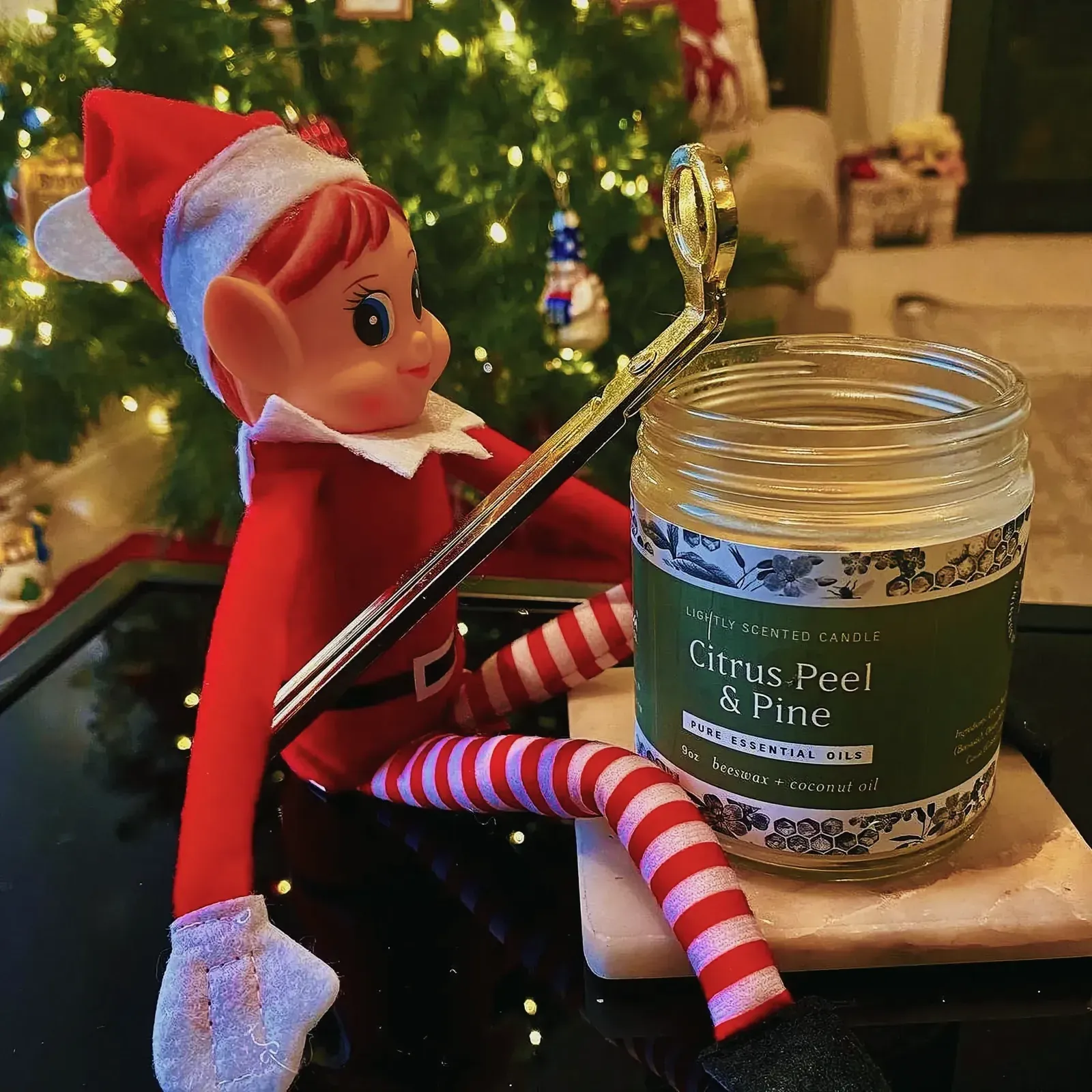 Festive scene featuring a toy elf playing a violin and a candle jar against a Christmas tree backdrop