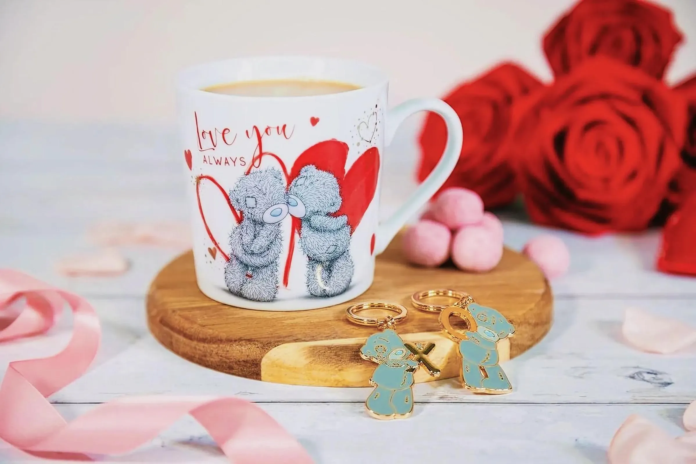 Ceramic coffee mug with teddy bears, gold earrings, and roses on a table
