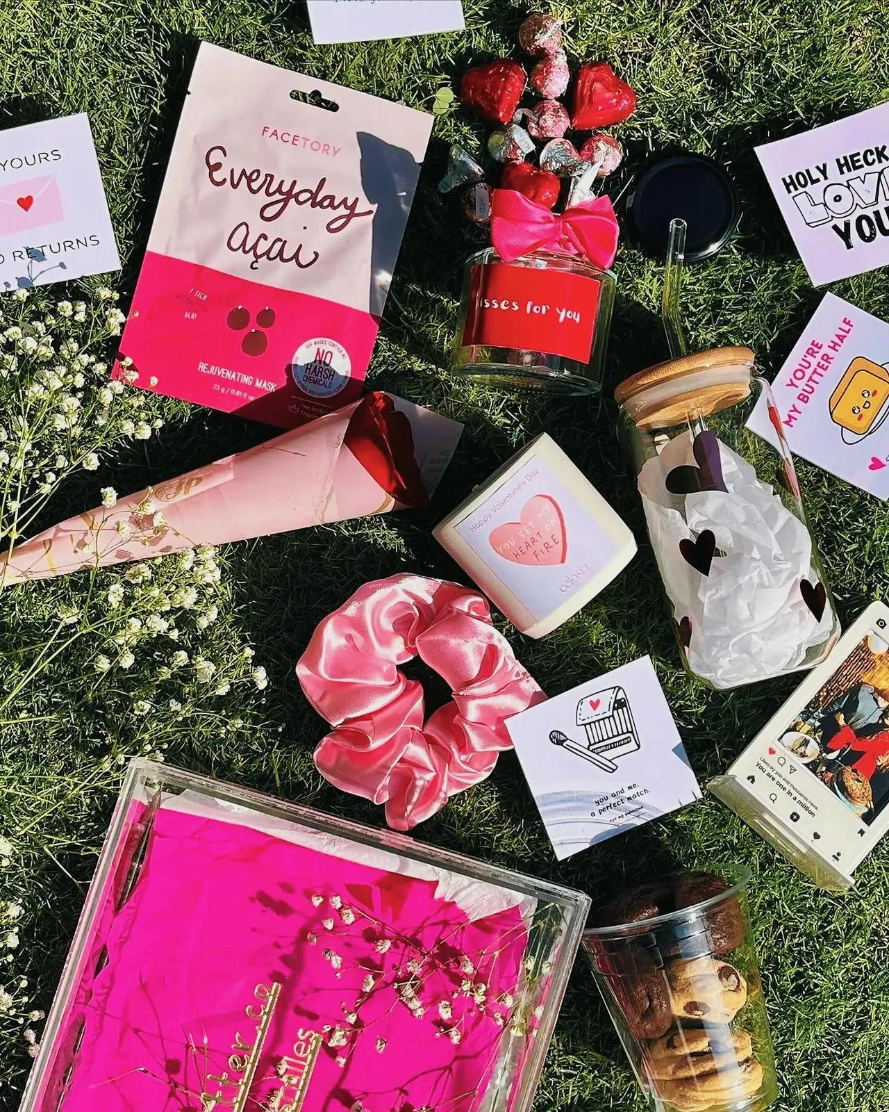 Valentine's Day gift box with cookies, scrunchie, and other items on a green grass backdrop